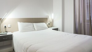 Una habitación de hotel con una cama grande, lámparas de noche, una mesita de noche y una ventana con cortinas.