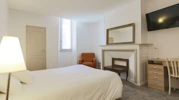 A hotel room with a bed, a chair, a desk, a television, and a fireplace.