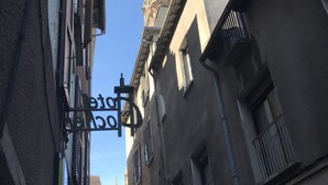 Una calle estrecha flanqueada por edificios, un letrero colgado de un poste, y un cielo azul despejado.