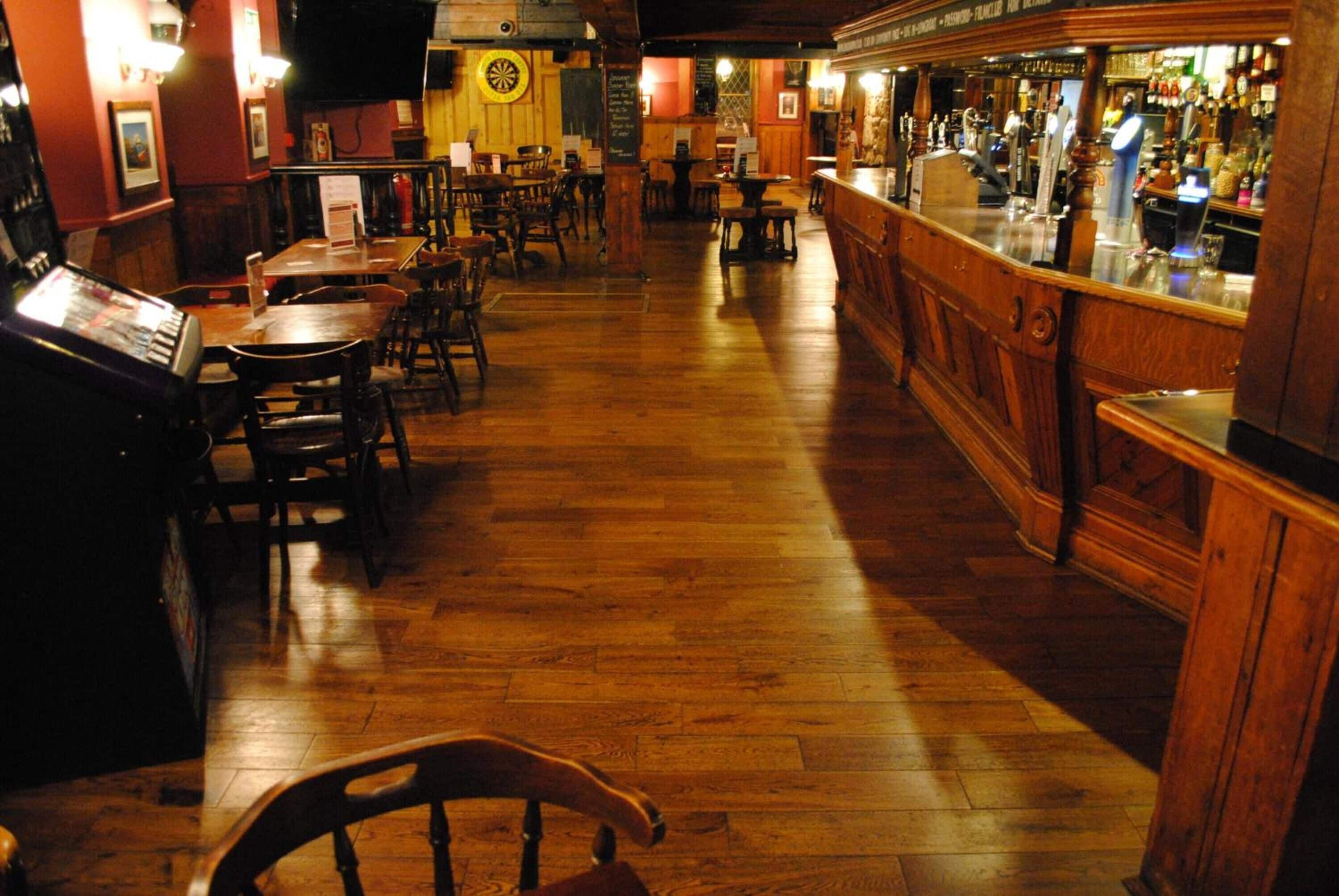 A bar area with wooden flooring, tables, chairs, and a bar counter.