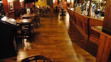 A bar area with wooden flooring, tables, chairs, and a bar counter.