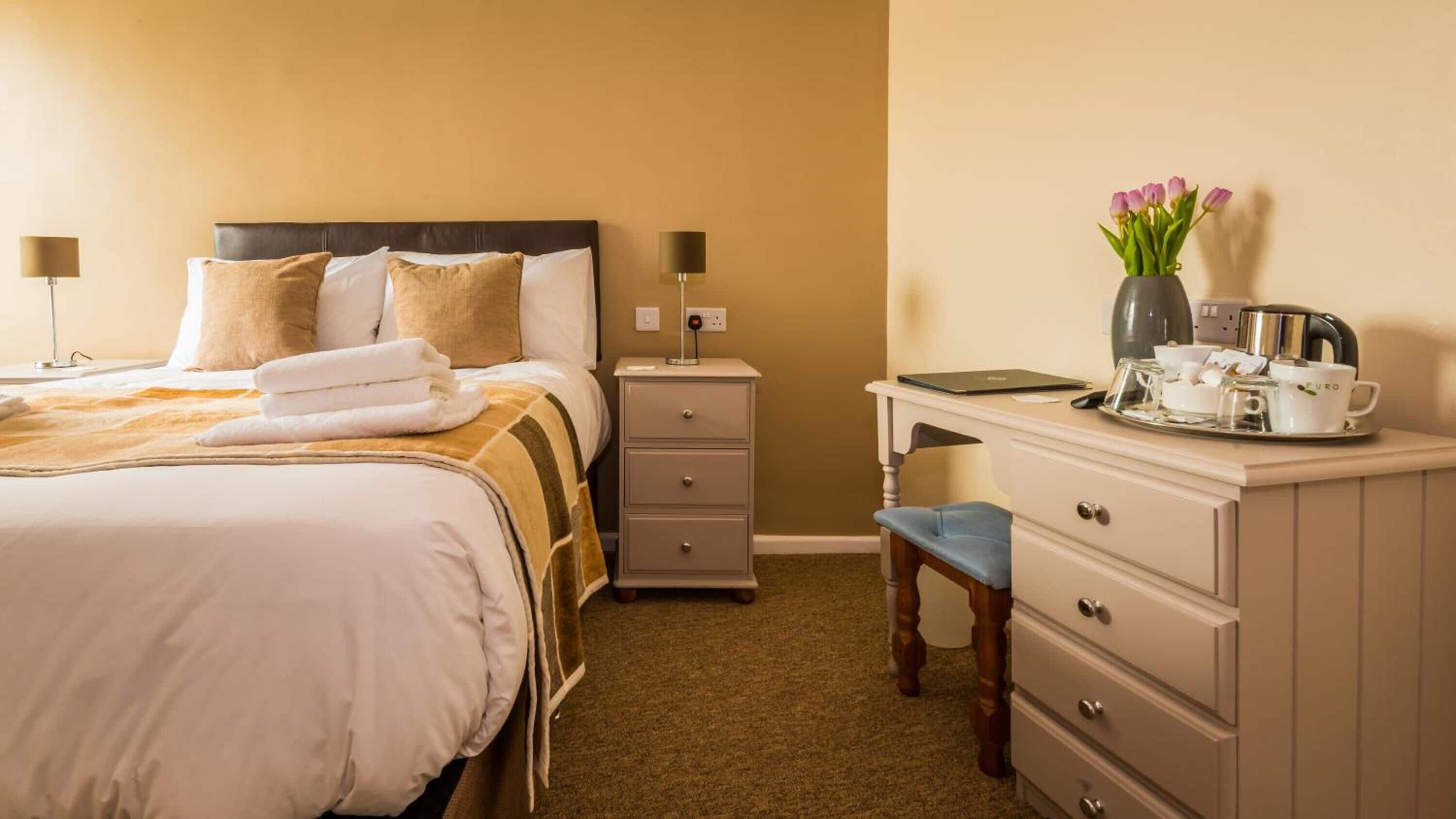 A hotel room with a bed, bedside tables, a desk, and a chair.