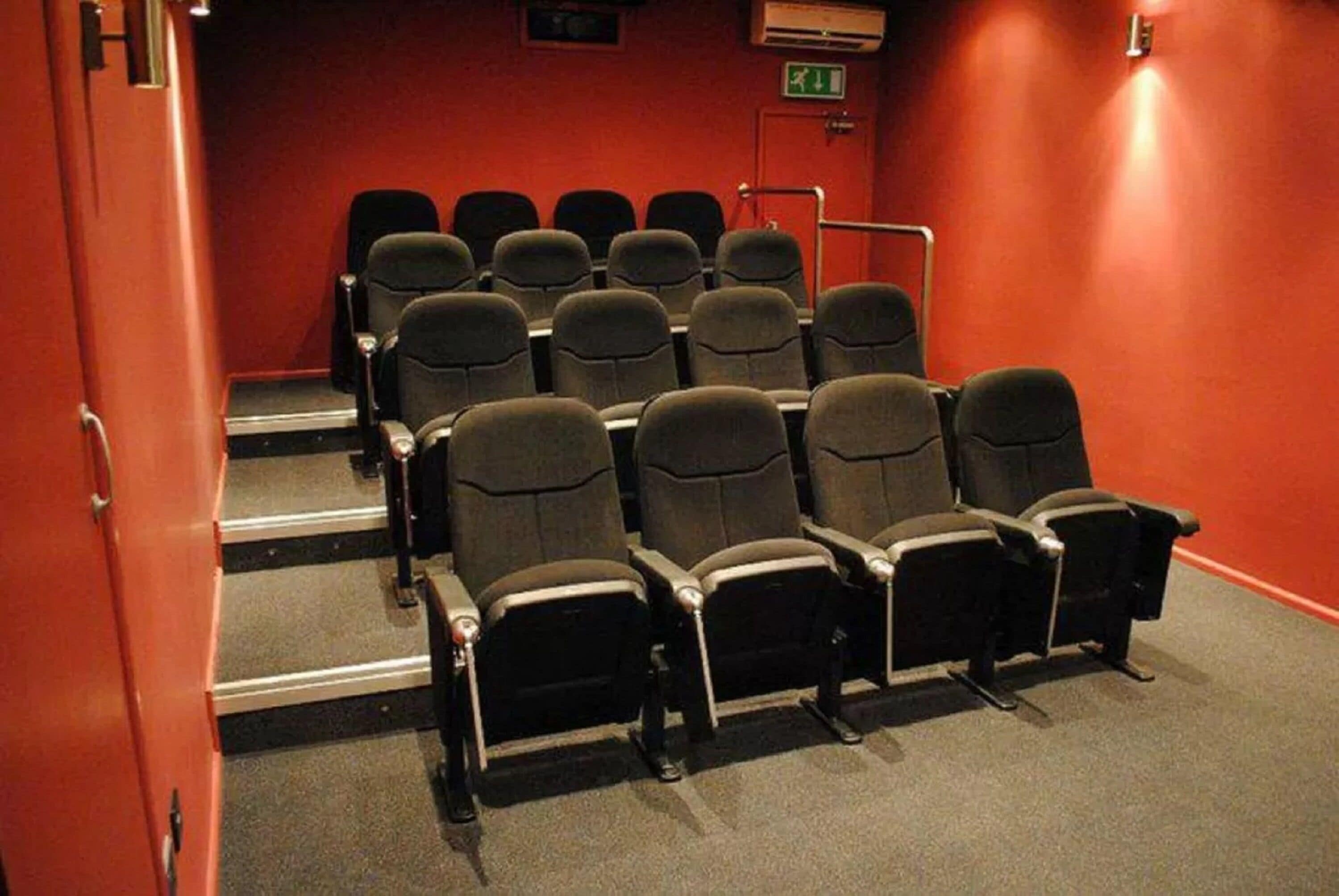 A theater with rows of black seats, a red wall, and a staircase leading to the seating area.