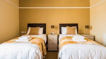 Ein Hotelzimmer mit zwei Einzelbetten, jeweils mit Kopfstütze, Nachttischen und Lampen.
