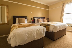 A hotel room with two beds, beige walls, and a large window with curtains.