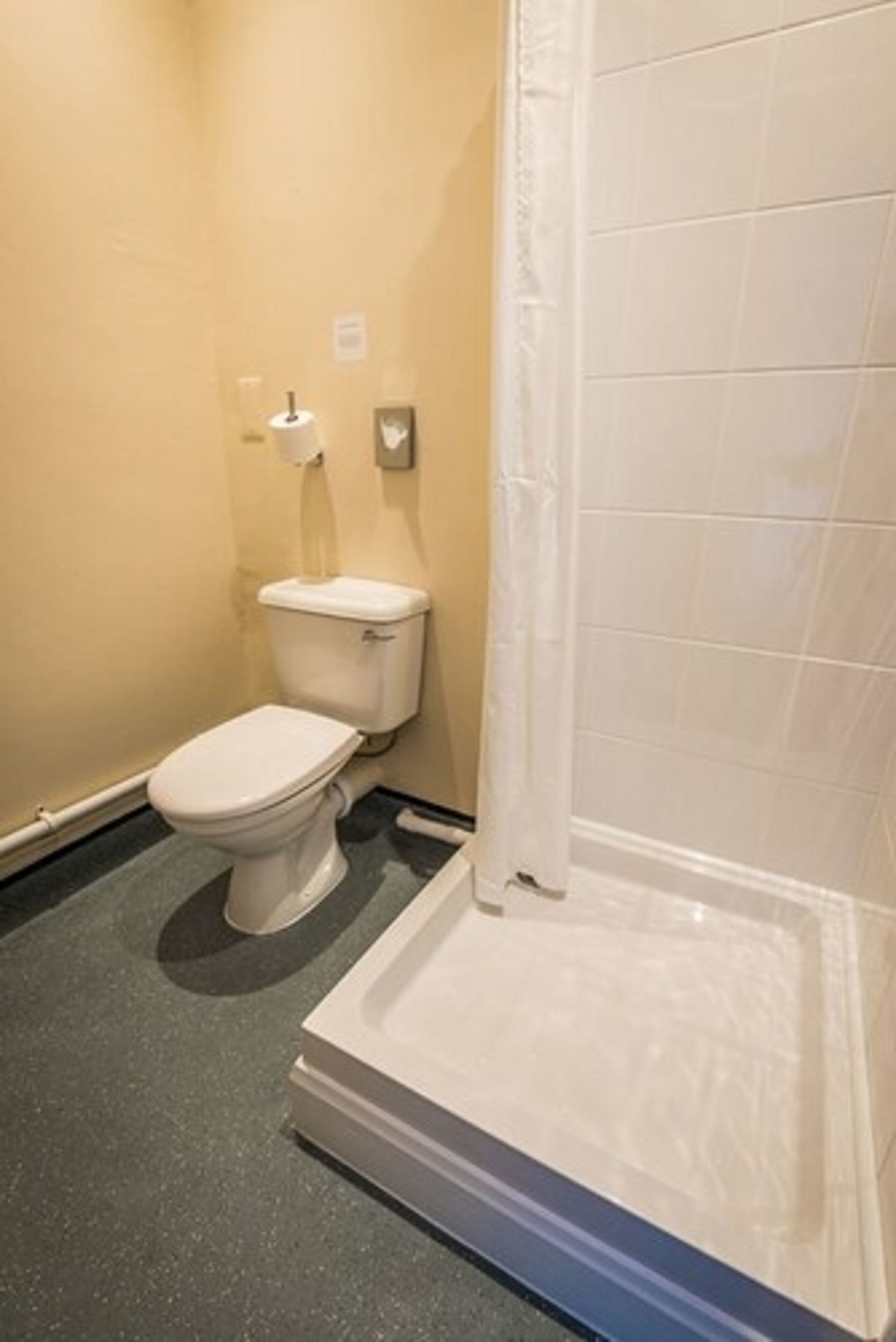 Ein kleines Badezimmer mit Toilette, Dusche und Toilettenpapierhalter.