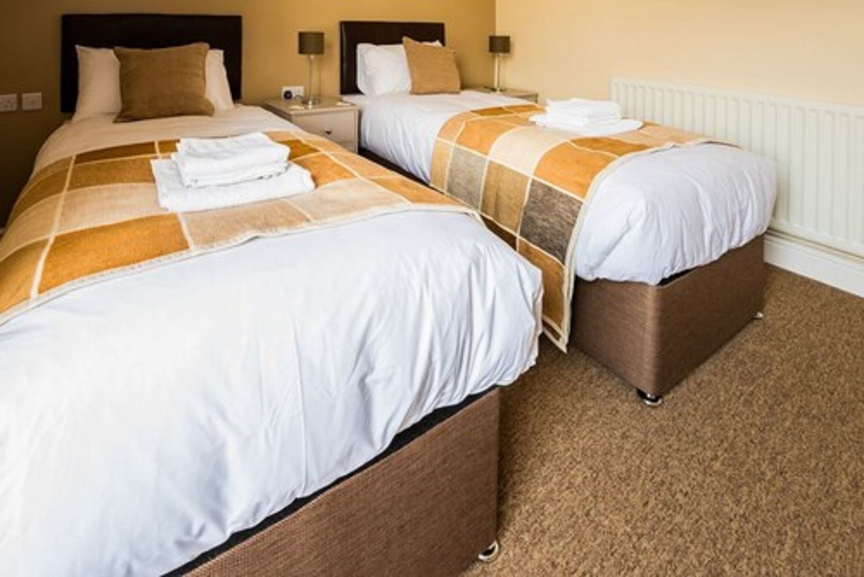 A hotel room with two beds, each with a brown headboard, white bedding, and a brown carpet.