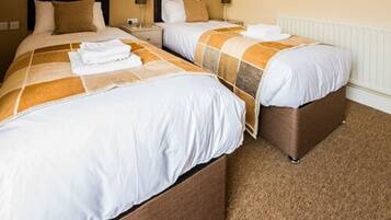 A hotel room with two beds, each with a brown headboard, white bedding, and a brown carpet.