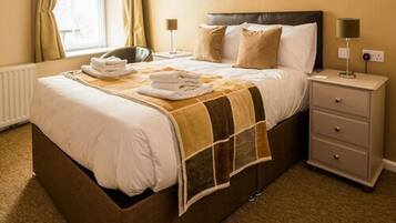 A neatly made bed with a brown headboard, a bedside table with a lamp, and a window with curtains.
