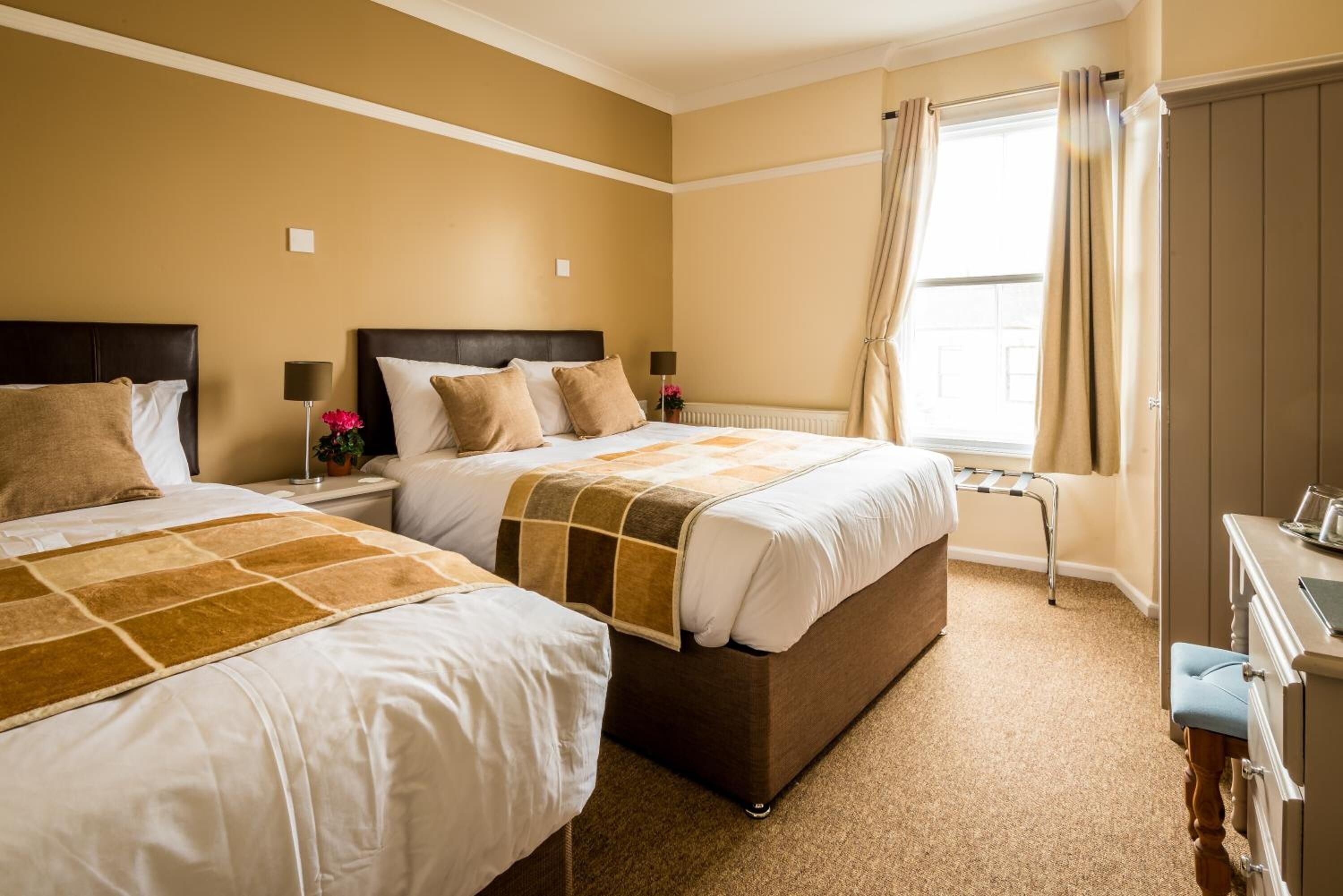 A hotel room with two beds, a desk, and a window with curtains.