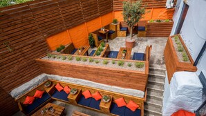 An outdoor seating area with wooden benches and tables, surrounded by raised planters with greenery. - The Longboat Inn (Penzance)