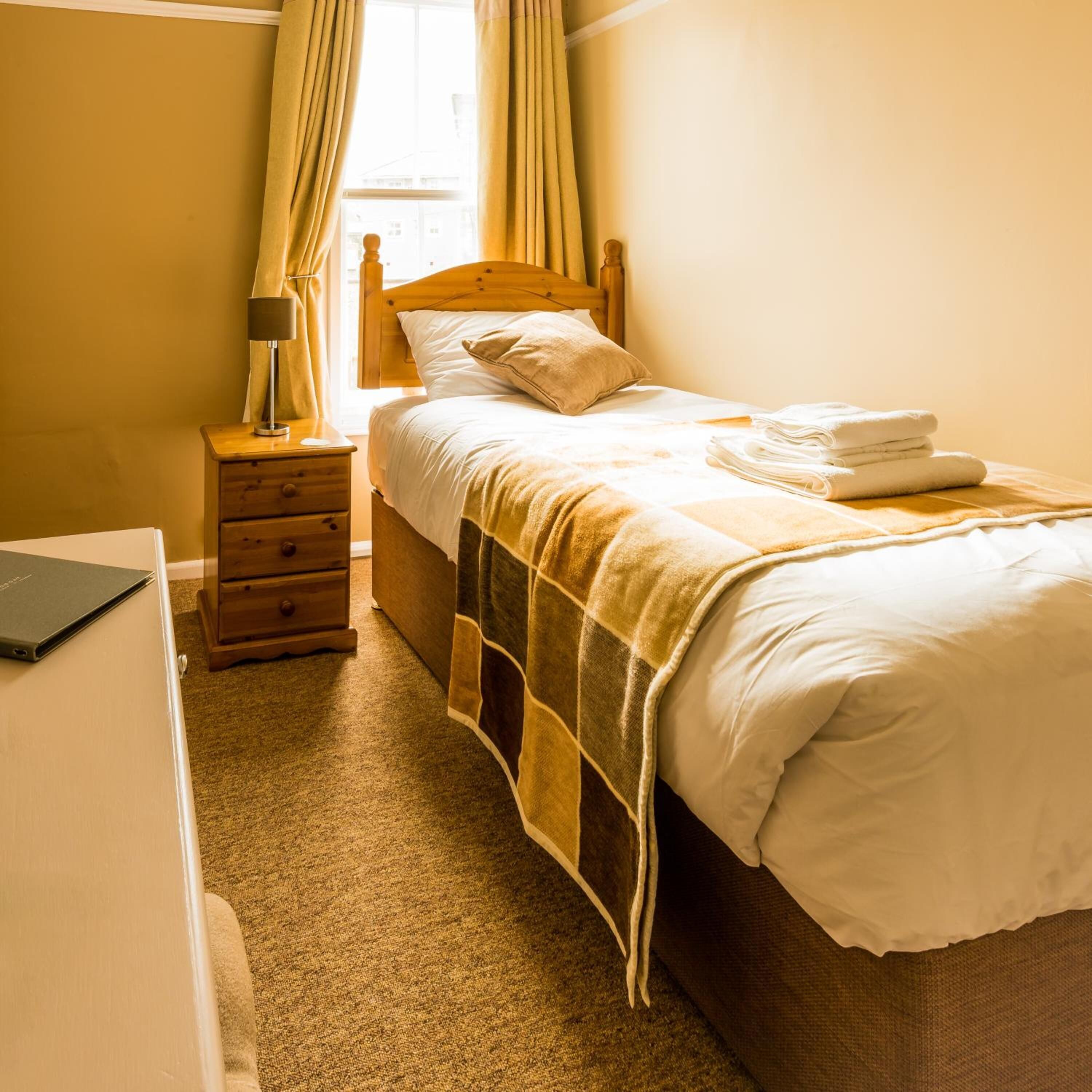 A bedroom with a wooden bed, a bedside table with a lamp, and a window with curtains.