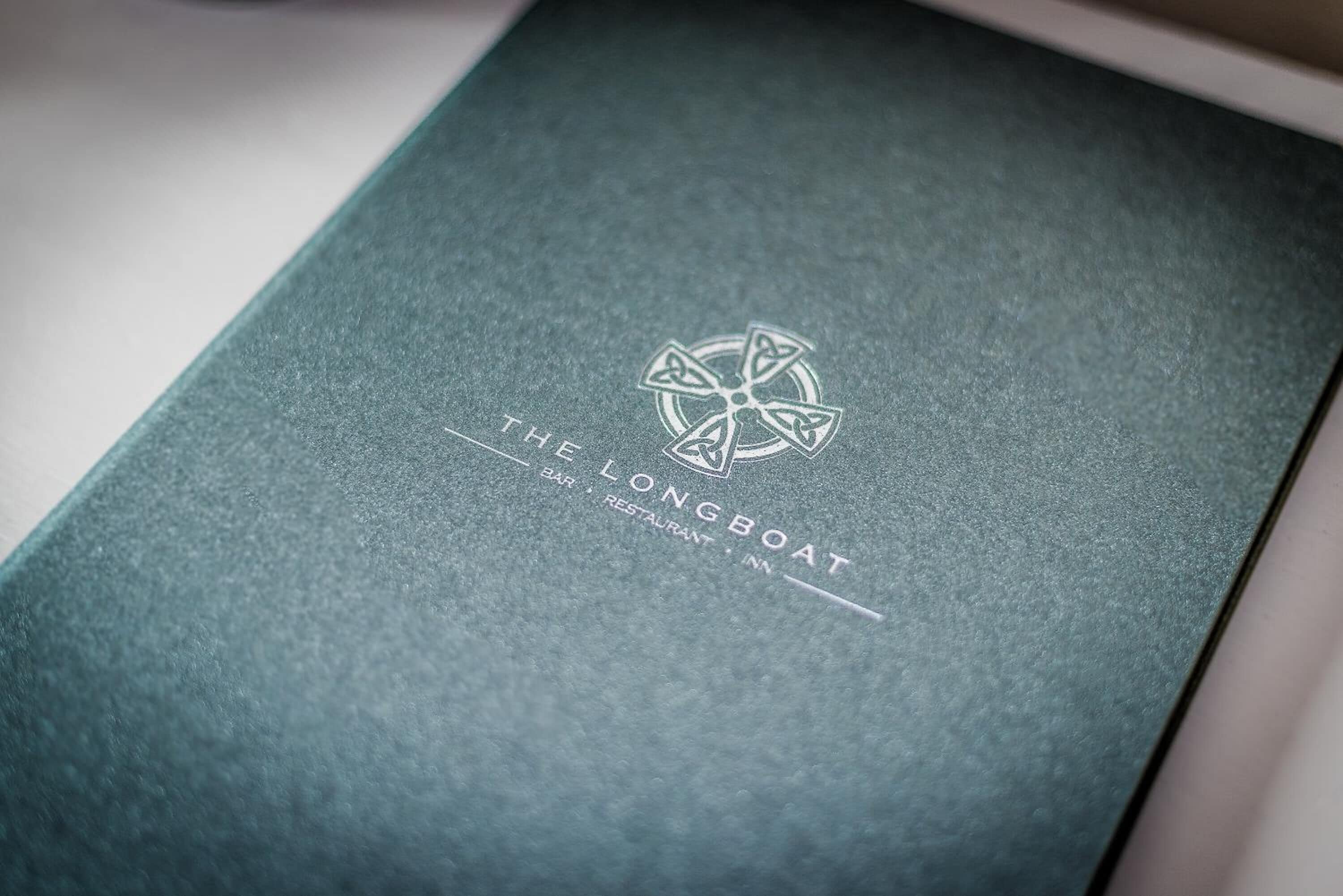 A dark green booklet with embossed text and a circular logo, indicating it is related to a bar, restaurant, and inn named "The Longboat."