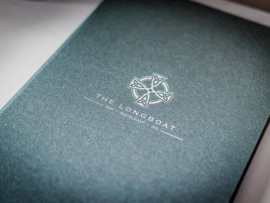 A dark green booklet with embossed text and a circular logo, indicating it is related to a bar, restaurant, and inn named "The Longboat."