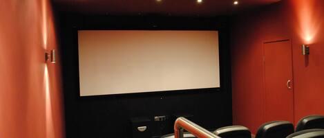 Un cine con una pantalla grande, filas de asientos negros y una pared roja.