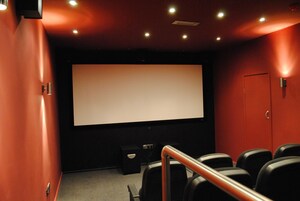 A movie theater with a large screen, rows of black seats, and a red wall.