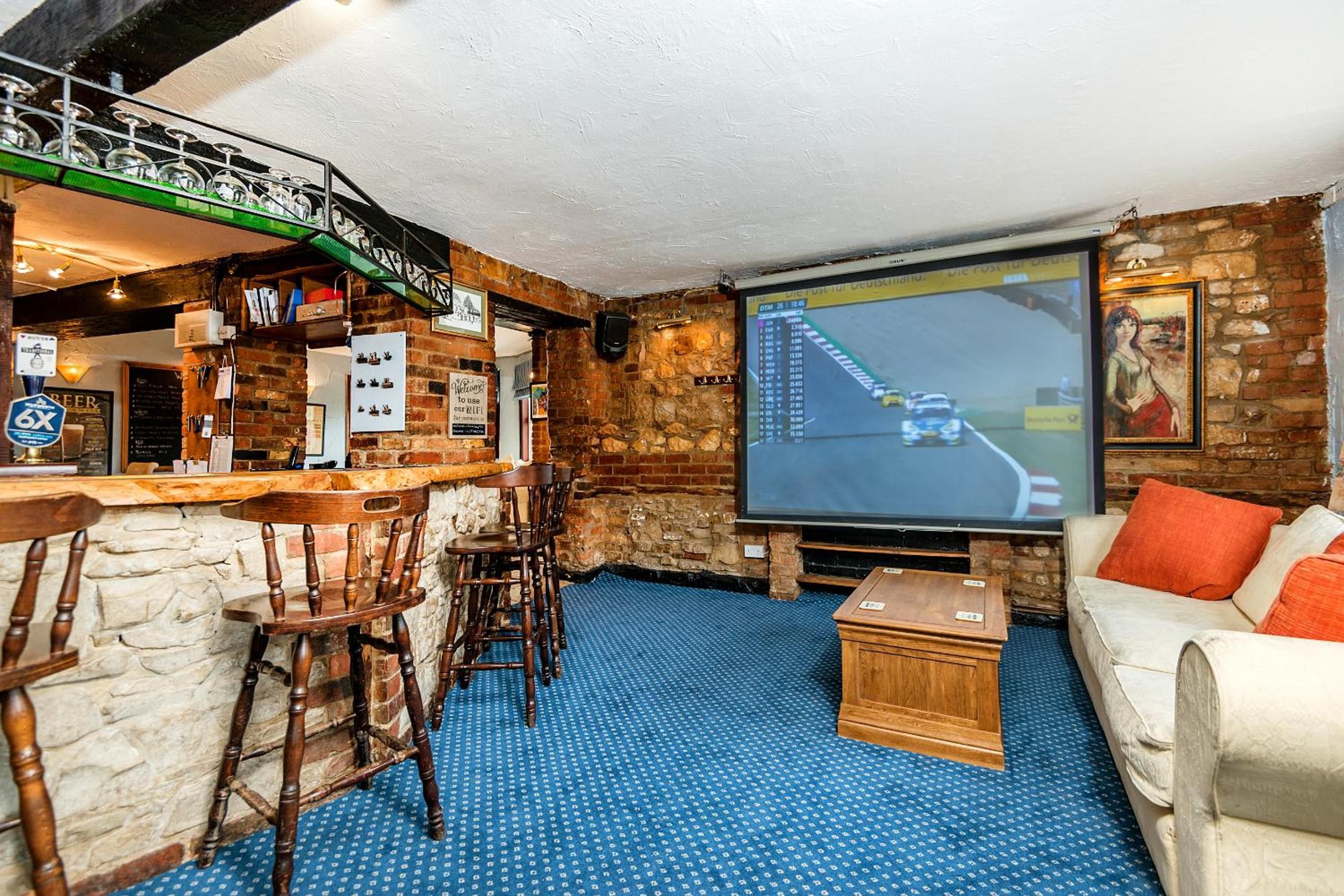 A bar area with a screen displaying a racing game, a stone wall, and a sofa with cushions.