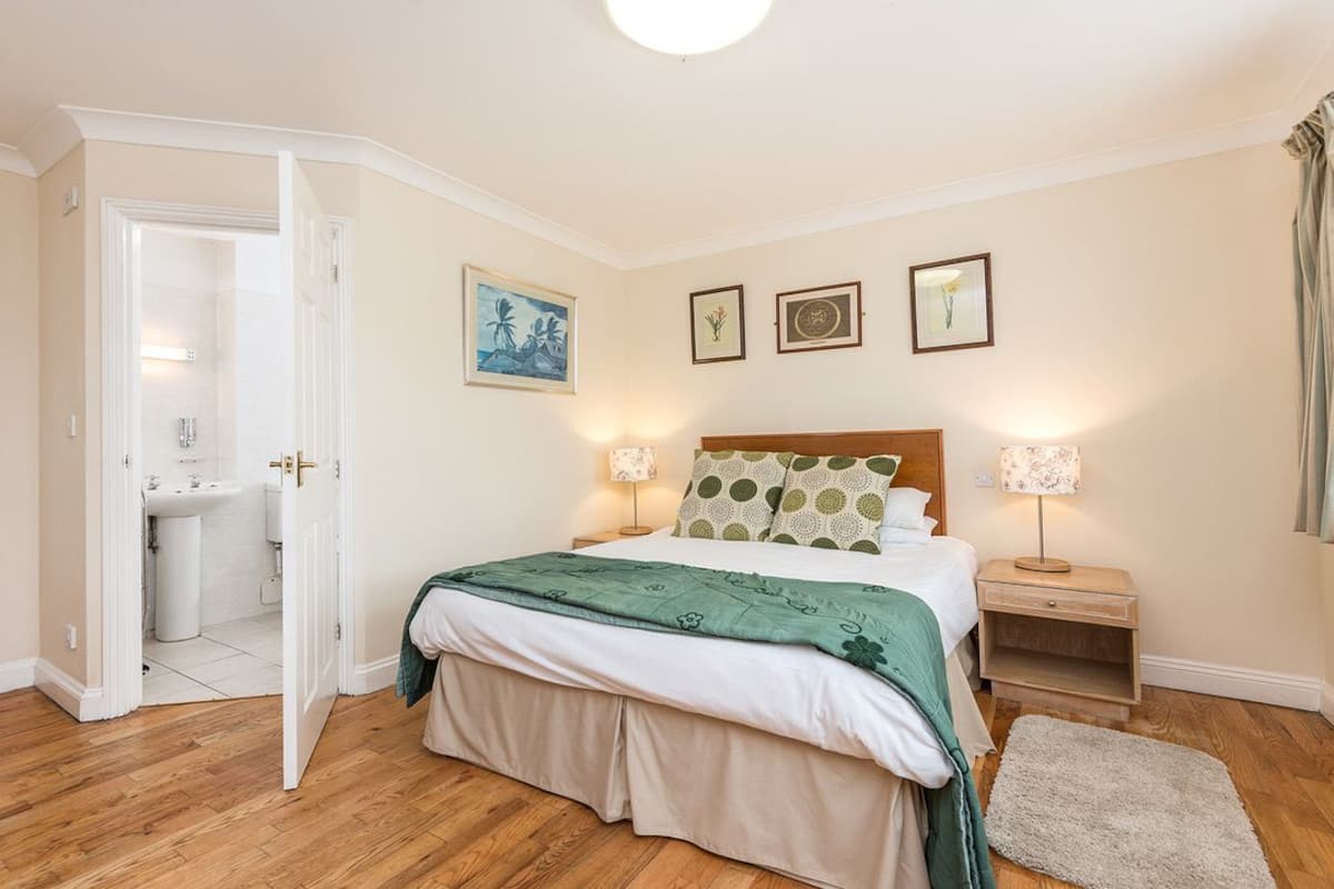 Un dormitorio con cama, mesitas de noche, una puerta al baño y obras de arte colgadas en la pared.