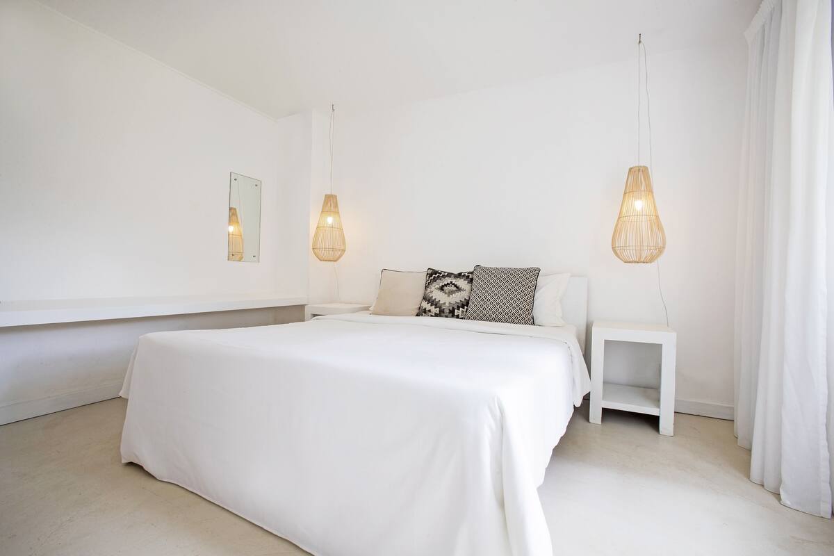 A minimalist bedroom with a large bed, two bedside tables, and hanging light fixtures.