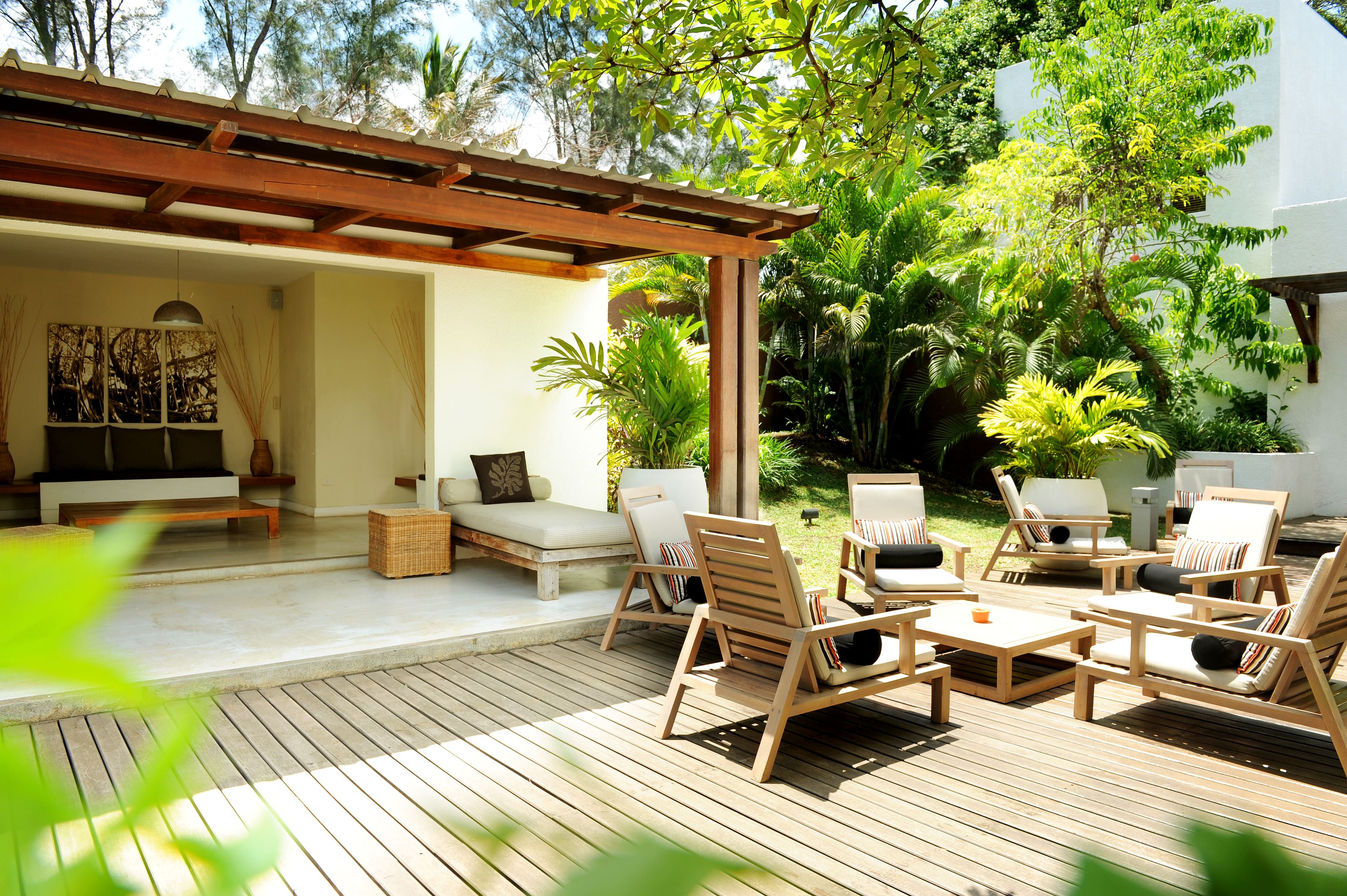 A wooden deck with outdoor furniture, including sofas and chairs, surrounded by lush greenery.