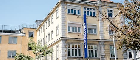 A multi-story building with a beige facade, multiple windows, and a red-tiled roof. A blue banner with the text "hostels.com" is visible.