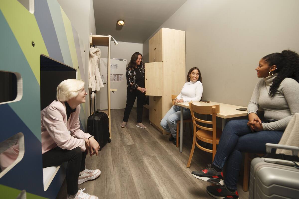 Ein kleiner, moderner Raum mit Holzboden, einem Tisch und Stühlen. Ein Kleiderschrank und ein Garderobenständer sind ebenfalls vorhanden.