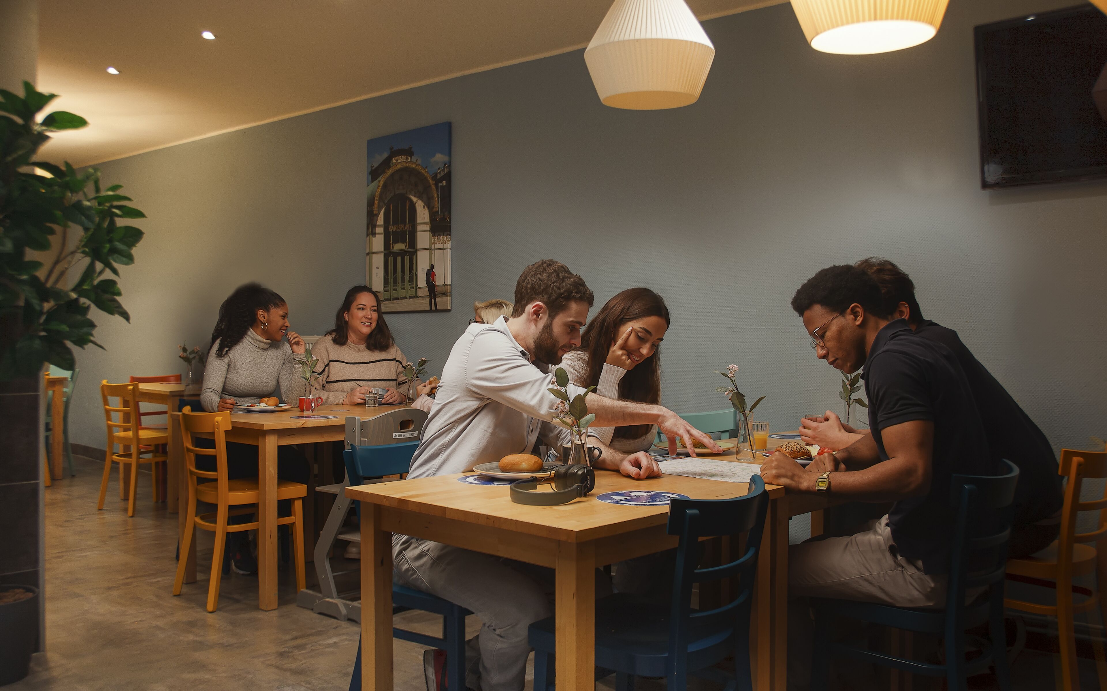 Eine Gruppe von Menschen speist in einem modernen Restaurant mit Holztischen und -stühlen, einem großen Fenster mit Aussicht und einem an der Wand befestigten Fernseher.