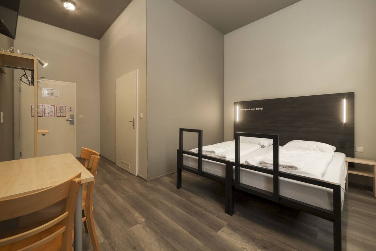 Ein kleiner, moderner Raum mit einem Einzelbett, einem Holztisch und einem Stuhl.
