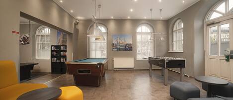 A modern indoor space with a pool table, foosball table, and seating areas.