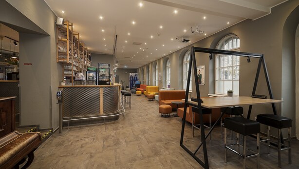 A spacious lounge area with seating, a bar, and a large window providing natural light. - a&o Wien Stadthalle (Vienna)