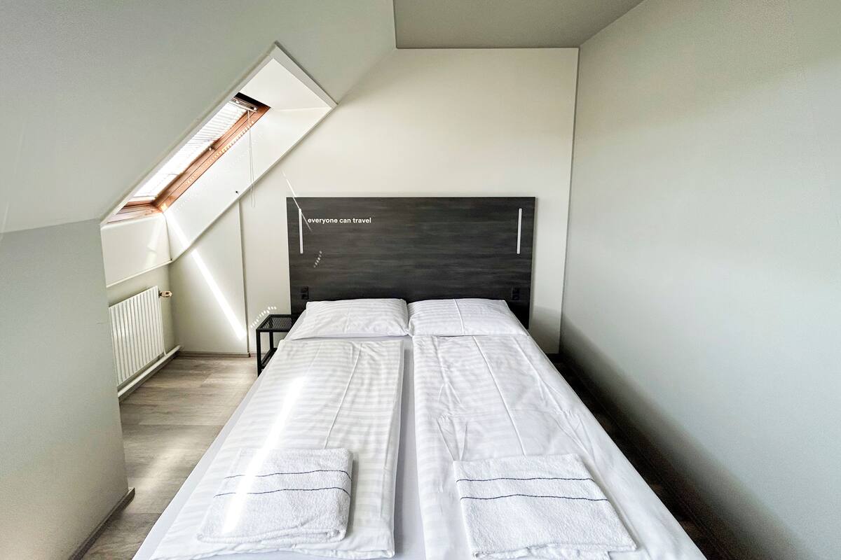 Ein schmales Zimmer mit einem Bett, einem Heizkörper und einem Oberlicht.