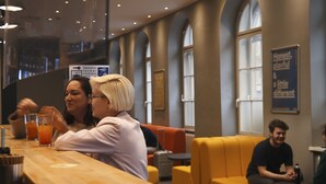 A modern interior with a long wooden counter, seating areas with yellow and orange chairs, and large windows. - a&o Wien Stadthalle (Vienna)