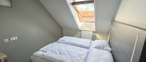 A small, modern bedroom with a skylight, a bed with white linens, and a radiator.