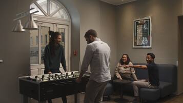 A room with a foosball table, a sofa, and a poster on the wall.