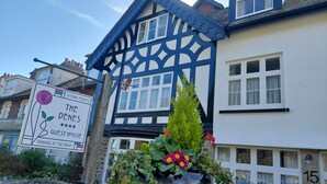 A traditional house with a blue and white exterior, a sign indicating it's a guest house, and a flower pot on the front. - The Denes Guest House (Lynton)