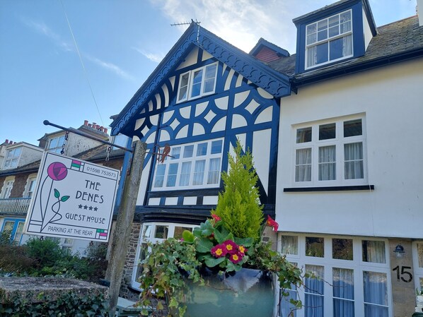 A traditional house with a blue and white exterior, a sign indicating it's a guest house, and a flower pot on the front. - The Denes Guest House (Lynton)