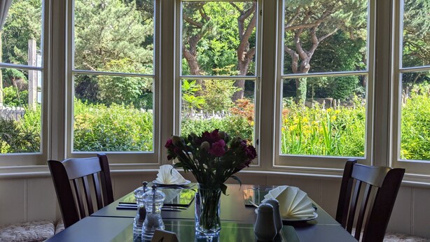 A dining table with a number 4 placemat, a vase with flowers, salt and pepper shakers, and a folded napkin. - The Denes Guest House (Lynton)