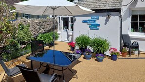 A patio area with a table and chairs, surrounded by potted plants and a white umbrella. - The Denes Guest House (Lynton)