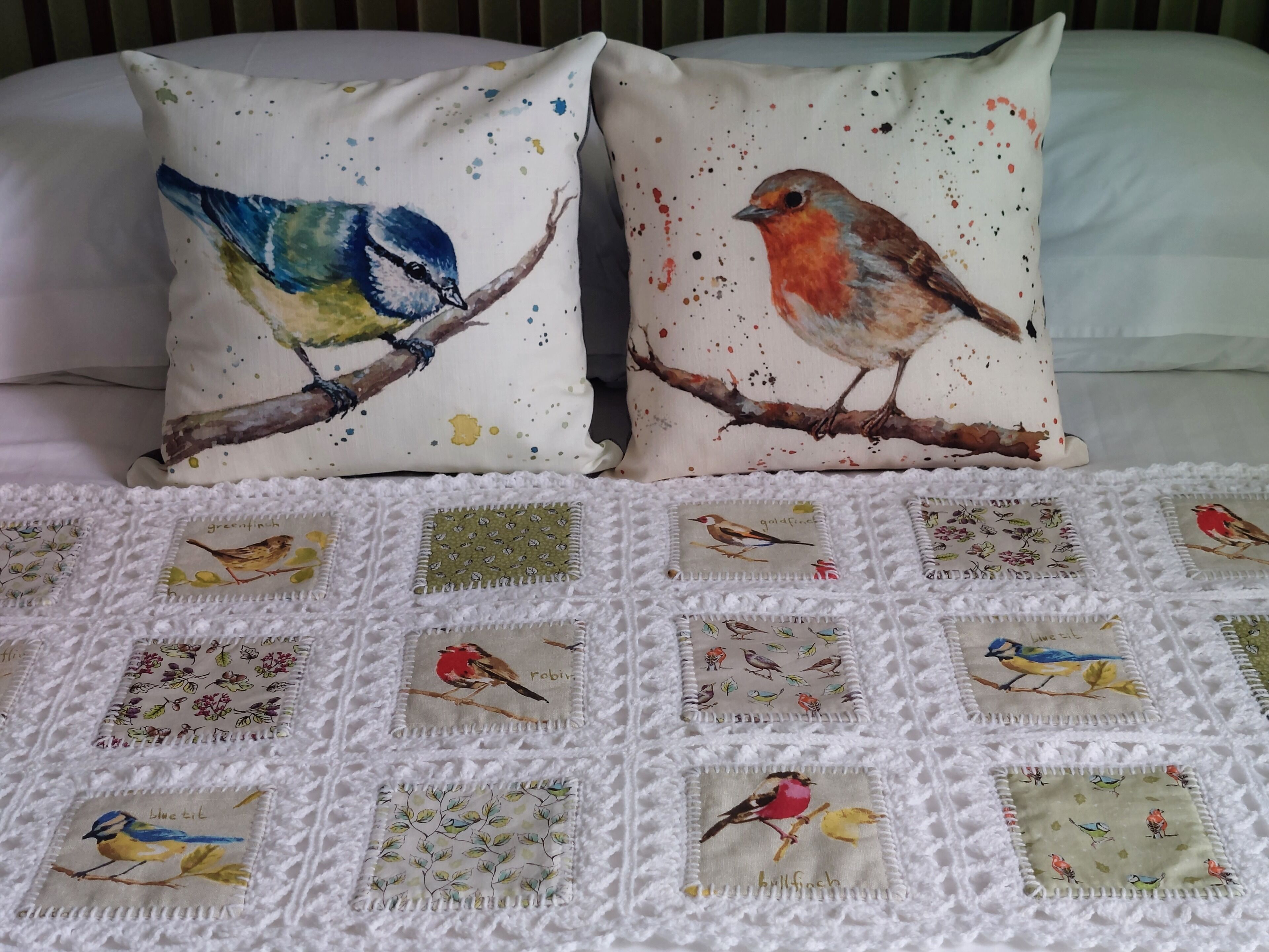 A bed with a white quilt featuring bird patterns and two pillows with bird designs.