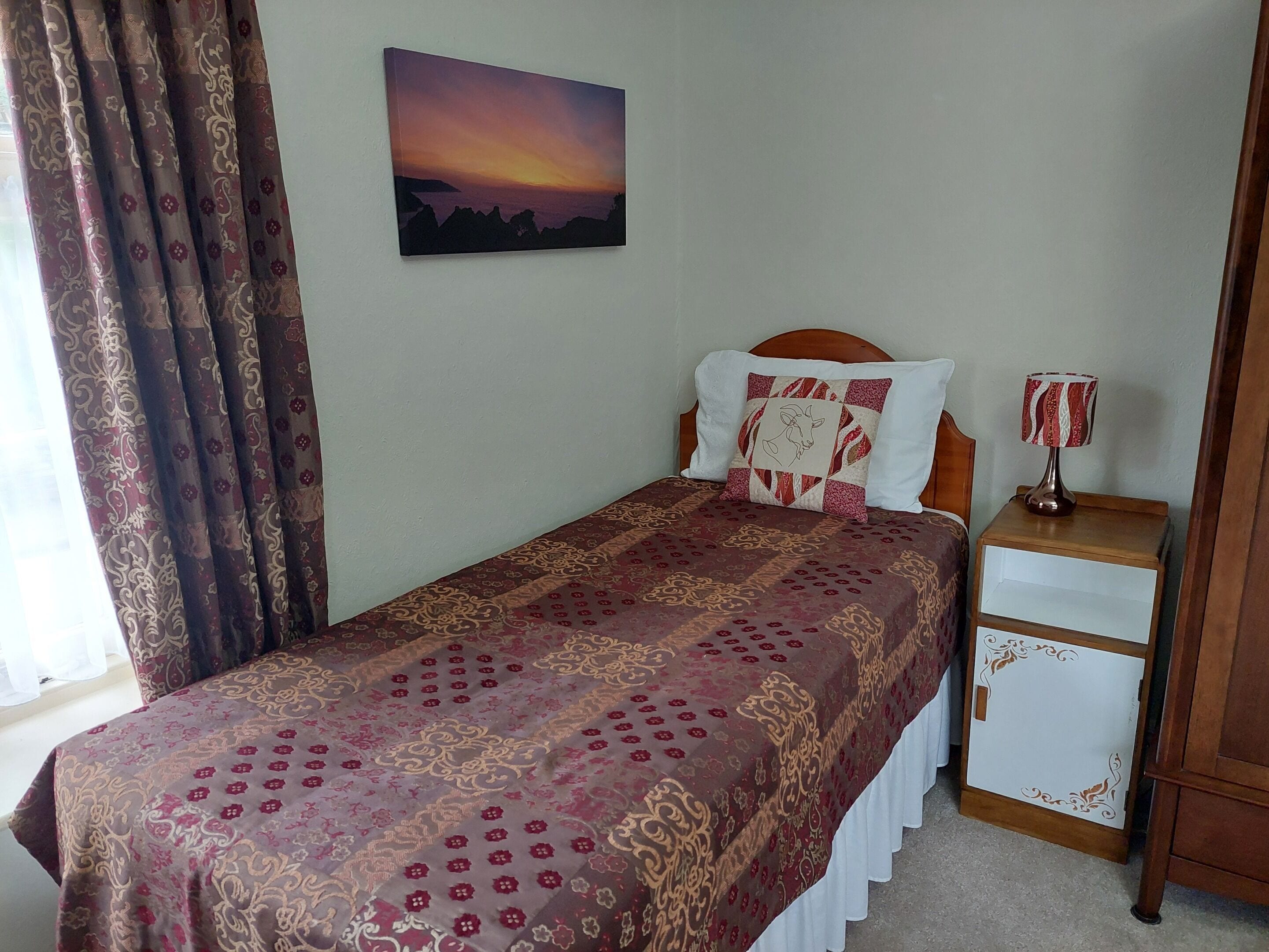 A neatly made bed with a patterned bedspread, a bedside table with a lamp, and a painting on the wall.