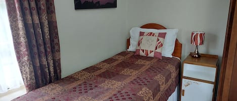 A neatly made bed with a patterned bedspread, a bedside table with a lamp, and a painting on the wall.