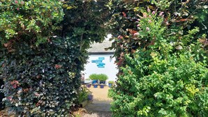 An entrance to a building with a gravel path leading to a white building with blue signage. - The Denes Guest House (Lynton)