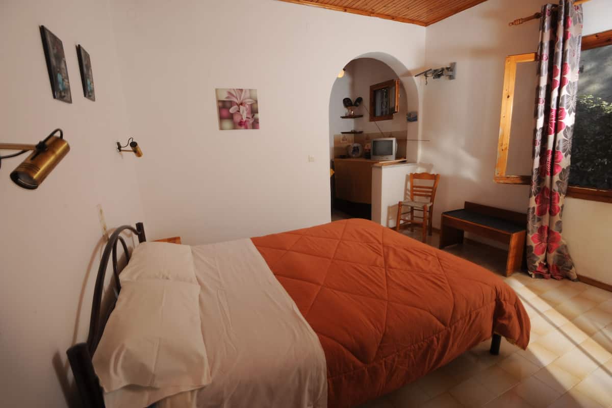 A bedroom with a bed, a desk, a chair, and a window with curtains.