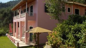 Une villa rose dotée d’un balcon, d’un espace salon extérieur abrité et d’un mur en pierre.