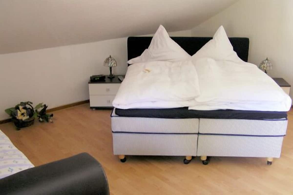A bedroom with a bed, nightstand, lamp, and a small plant.
