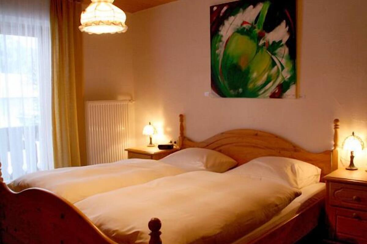 A double bed with wooden headboard and footboard, two bedside tables with lamps, a radiator, and a painting on the wall.