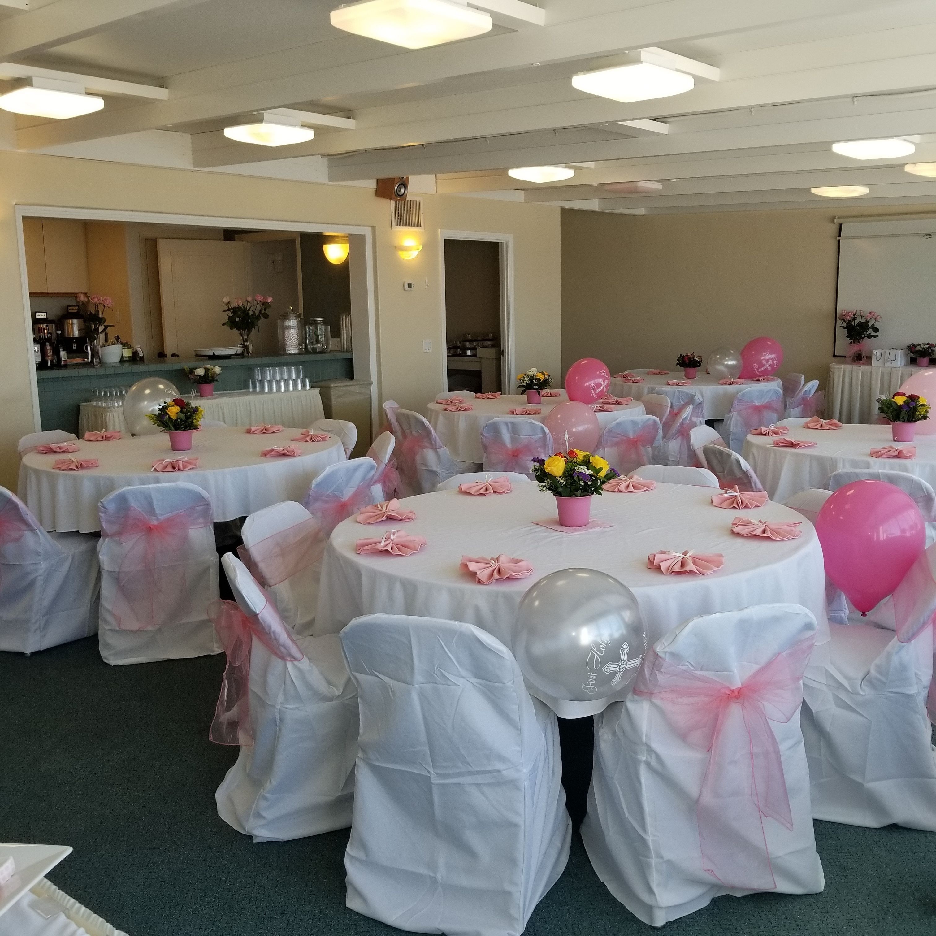 Une salle de banquet avec des tables rondes, des nappes blanches et des chaises ornées de rubans roses.