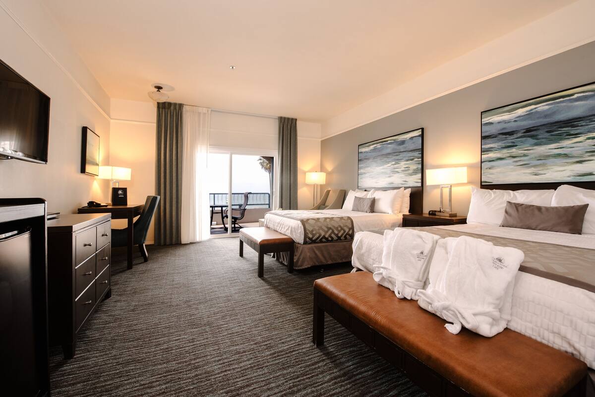 Habitación de hotel con cama, escritorio, silla, banca y vistas al exterior.