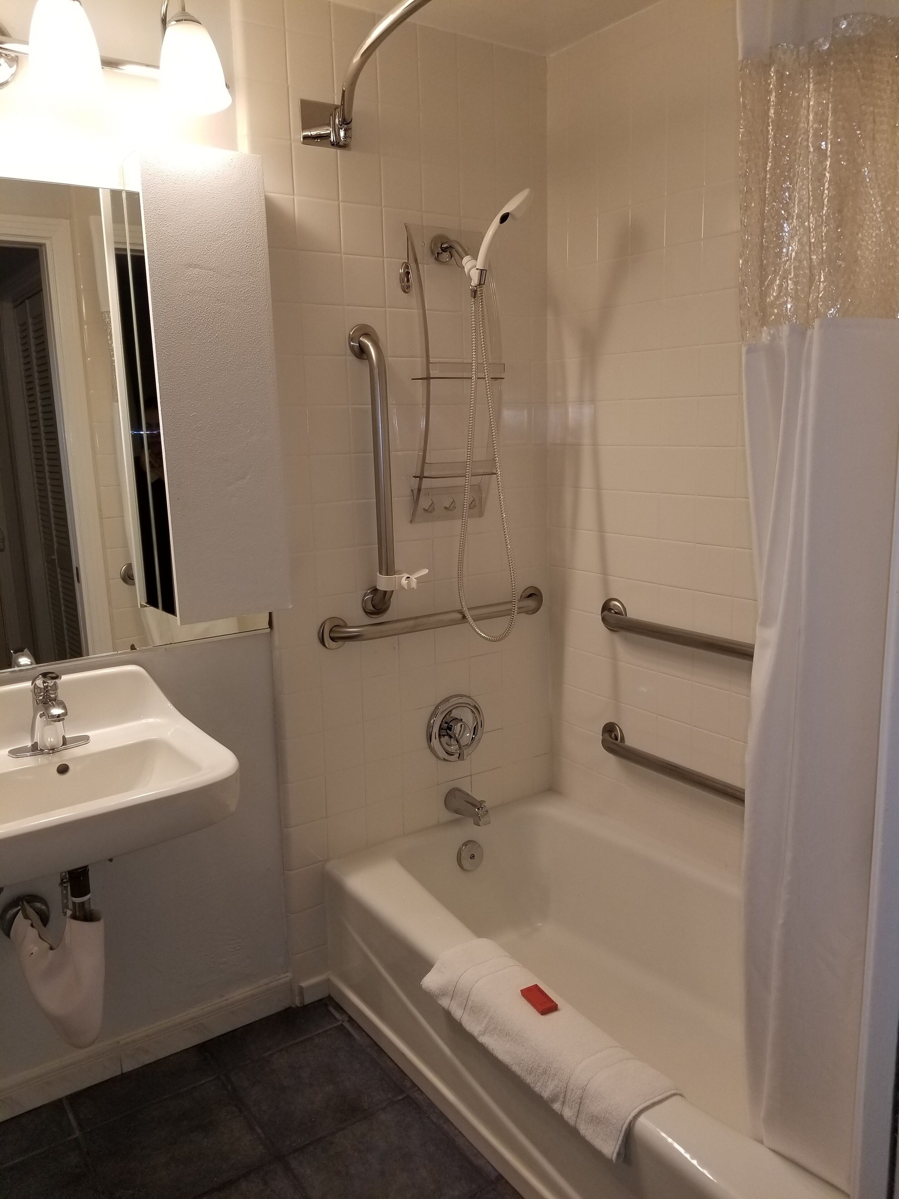 Un baño con lavamanos, ducha con barras de apoyo y toallero.