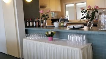A kitchen area with a counter displaying wine bottles, a vase with flowers, and a table covered with a white cloth.
